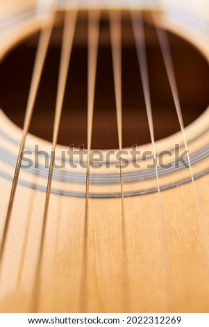 Detail of the body of a light wood electroacoustic guitar, the soundhole and strings. Close-up vertical image with shallow depth of field.