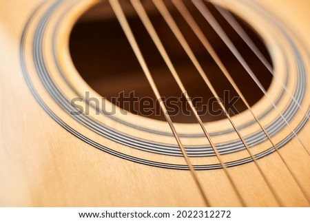 Detail of the body of a light wood electroacoustic guitar, the soundhole and strings. Close-up horizontal image with copy space and shallow depth of field.