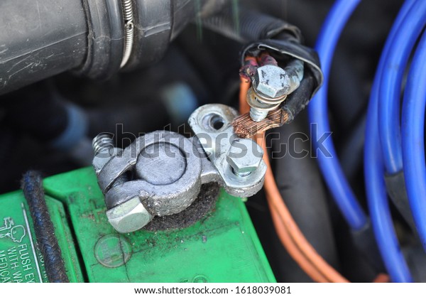 Detail of car battery positive post. Battery is\
bungied in place. Battery cable is falling apart and held together\
with duct tape.
