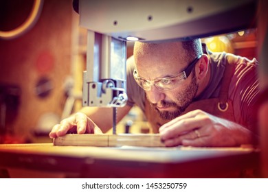 detail of a carpenter at work cutting a plank with a band saw in his workshop, Caucasian with a beard and protective glasses. - Powered by Shutterstock