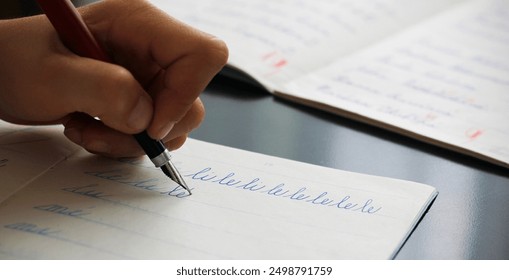 Detail of a child's left hand writing the syllables li and le with a fountain pen in a copybook. Concept for writing with the left hand. Back to school concept. Retro school writing in cursive.