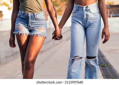 detail of the clasped hands and legs of a couple of unrecognizable black girls walking holding hands, concept of love and friendship, copy space for text