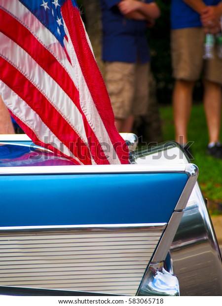 Detail of a classic car with an American\
flag attached driving in a Fourth of July Parade.\
