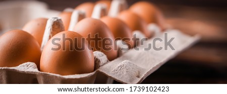 Detail close-up of chicken eggs in egg box on the old brown wooden background.
