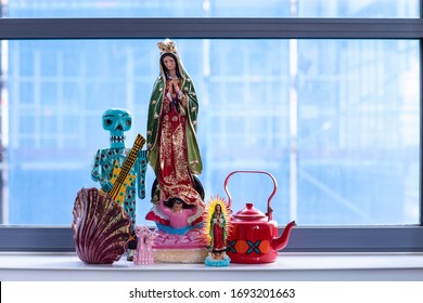A detail of a collection of colourful statues set a city loft interior. A bohemian, modern, mix and match eclectic styled home with our lady Guadalupe praying and a wooden Mexican skeleton. deco