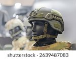 Detail of a composite image showcasing three soldier helmets, with central focus on a helmeted figure wearing protective eyewear and additional equipment straps Secondary images blurred profiles o