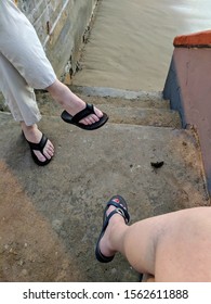 Detail Of A Couples Sandaled Feet While Sitting On A Beach Wall Deep In Conversation.