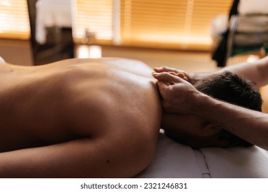 Detail cropped shot of professional male massage therapist making relaxed client muscular athlete man neck massage in dark cozy spa massage salon. Professional sports massage after training. - Powered by Shutterstock