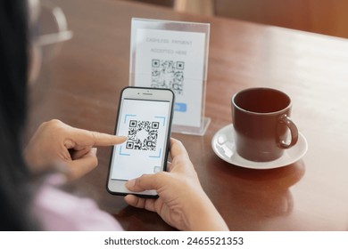 Detail of customer hand making payment through smartphone and scan code at cafe. Asian woman paying with QR code. Back view, selective focus. - Powered by Shutterstock