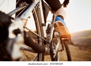 Detail of cyclist man feet riding mountain bike on outdoor trail in sunny meadow