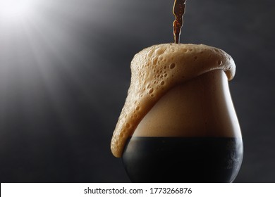 Detail of dark beer with overflowing foam head. Stream of dark stout pours into a beer glass	