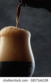 Detail Of Dark Beer With Overflowing Foam Head. Stream Of Dark Stout Pours Into A Beer Glass