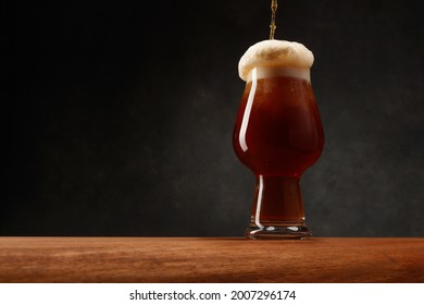 Detail Of Dark Beer With Overflowing Foam Head. Stream Of Dark Stout Pours Into A Beer Glass. Selective Focus
