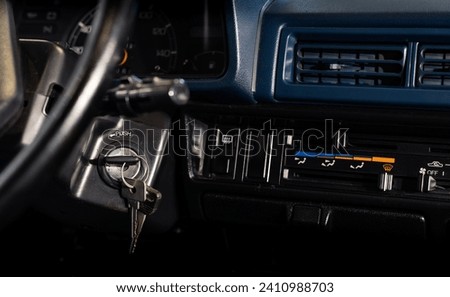 A detail from the dashboard of an old-fashioned car, with the ignition key inserted into the lock.