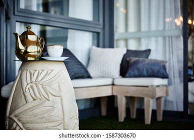 Detail Of A Decorated Inner City Apartment Balcony With Settees, Cushions And A Cup Of Tea And Tea Pot On A Side Table In Foreground