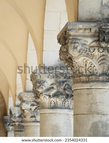 detail of an decorated or ornamented capital or chapiter column or pillar in a row with others next to each other in a hall with arches as historic and antique background design
