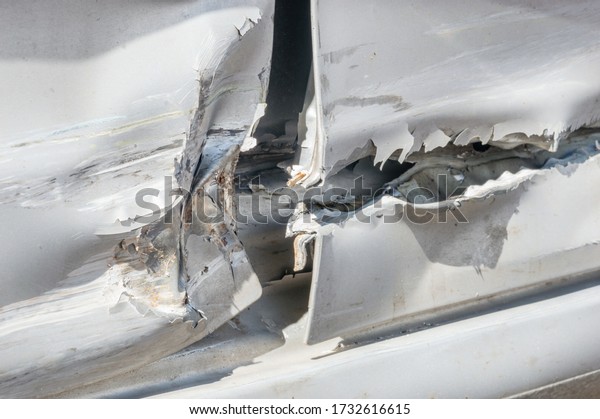 Detail of dented and torn\
sheet metal on the side of the silver car doors damaged in crash\
accident.