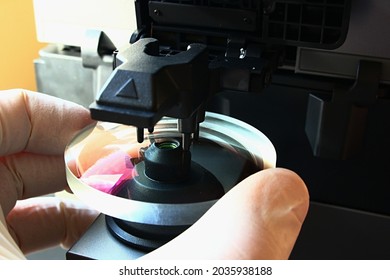 Detail of digital lensmeter measurement  of high end antireflex uncut round eyeglass lens with pink tint, used for filtering of HEV blue light. Lens is held by optician hand in sterile latex glove.