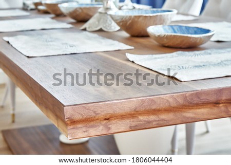 Detail of dinner table made of solid walnut wood on massive legs and served with plates. Blurred background
