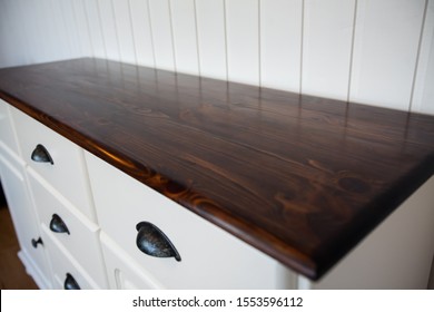 Detail Of A Dresser. Top And Front Are Visible. The Top Is Dyed In Dark Brown With A Mirror Finish And The Front With The Doors And Drawers Are In Pure White With Black Hardware.