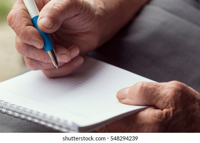 Detail Of An Elderly Woman's Hands Holding A Pen And Writing A Grocery List. Selective Focus