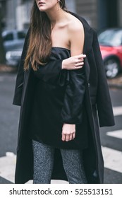 detail of a fashionable woman wearing a black oversized coat, an off the shoulder silk satin dress and glitter pants