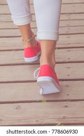 Detail of female feet in sneakers while walking on a wooden post.