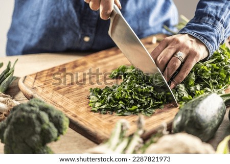 Detail of female hands holding a knife and chopping fresh parsley greens.