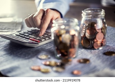 Detail Of Female Hands Wokring With Calculator Next To Two Jars Full Of Coins.