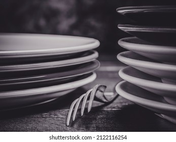 The detail of a fork between two piles of stacked plates, in black and white