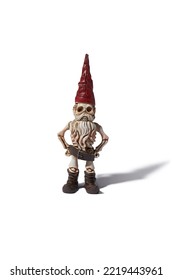 Detail Front Shot Of A Designer Figurine Of A Skeleton Of A Dwarf Man In A Red Hat And A Brown Loincloth. The Original Handmade Statuette Is Isolated On The White Background.                          