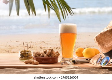 Detail of glass of beer fresh on wood  in the sand along with a succulent snack on a beach with palm tree on a hot day