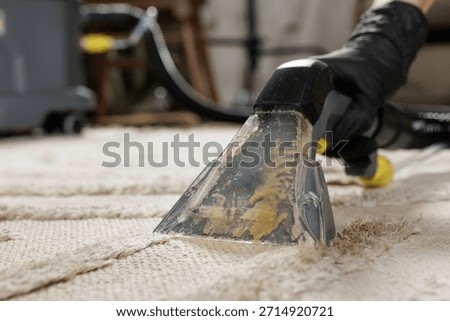 Detail of gloved worker using extraction nozzle to pull dirty solution from beige carpet surface