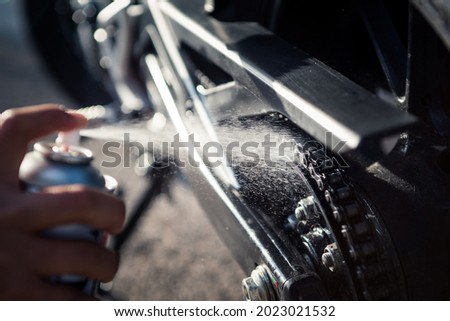 Detail of hand applying spray lubricant on motorcycle chain. Close-up photograph of oil droplets splashing.