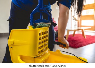 Detail Of Hand Of Latino Janitorial Worker Lady In Blue Uniform Draining The Water From A Mop In A Yellow Mopping Cart