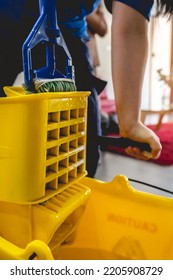 Detail Of Hand Of Latino Janitorial Worker Lady In Blue Uniform Draining The Water From A Mop In A Yellow Mopping Cart