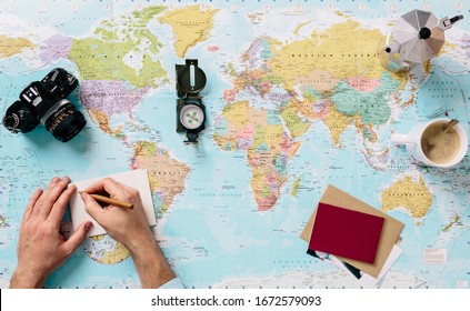 detail of a hand on a world map, writing in a notebook with a pencil the itinerary of his next travel destination. Horizontal image with space for text