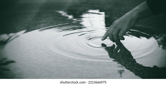 Detail of a hand touching lake water surface leaving ripples in concentric circles. People in nature. Unity, harmony and mindfulness concept. Monochrome panorama banner with copy space