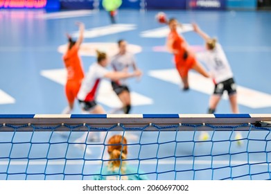 Detail of handball goal crossbar with net and women handball match in the background.