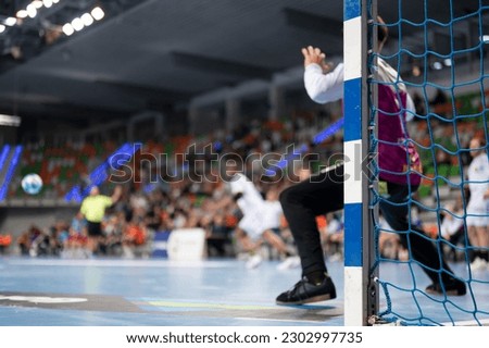 Detail of handball goal post with net and players in the background.