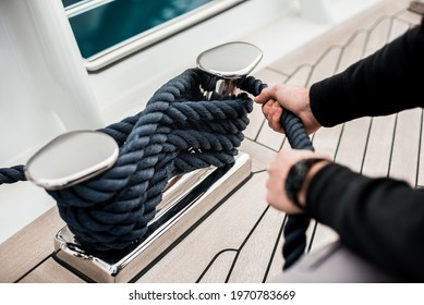 Detail of hands cleating off superyacht mooring lines on the foredeck with teak deck and stainless steel fittings - Shutterstock ID 1970783669