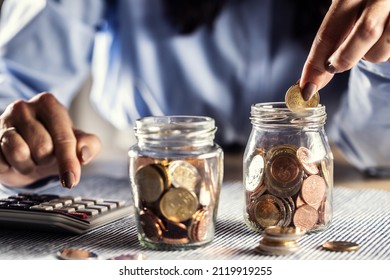 Detail Of Hands Counting Coins In Two Jars On A Calculator.