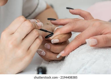 Detail Of The Hands Of A Manicurist Painting The Nails With A Black Nail Polish. Designing And Beautifying The Nails Of A Woman Who Is In The Beauty Salon. Varnishing The Nails. Dark Style.