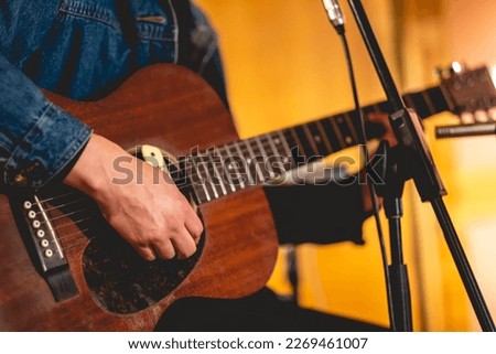 Detail of hands of rocker musician playing a wood electro acoustic guitar in a music studio