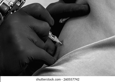 detail of the hands of a tattoo artist tattooing the back of a young woman in the tattoo cabin at his tattoo shop - focus on the needle