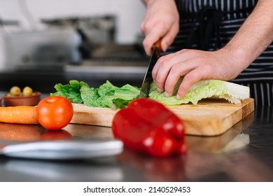 detail of the hands of a young chief man, cutting lettuce in a professional kitchen on a cutting board. - Shutterstock ID 2140529453