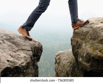 Detail of  hiker legs in black orange hiking boots on mountain summit. Feet in trekking shoes and legs  light trousers  on background of the peaks