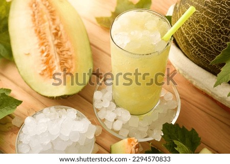 Detail of iced melon drink in a glass on a wooden table with fruit and crushed ice. Elevated view. Horizontal composition.