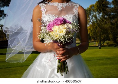 Detail image of an African American bride holding her rose bouquet in front of her.  Her veil blows gently in the wind.