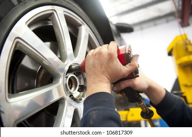 Detail Image Of Mechanic Hands With Tool, Changing Tyre Of Car, With Blurred Background Of Garage.